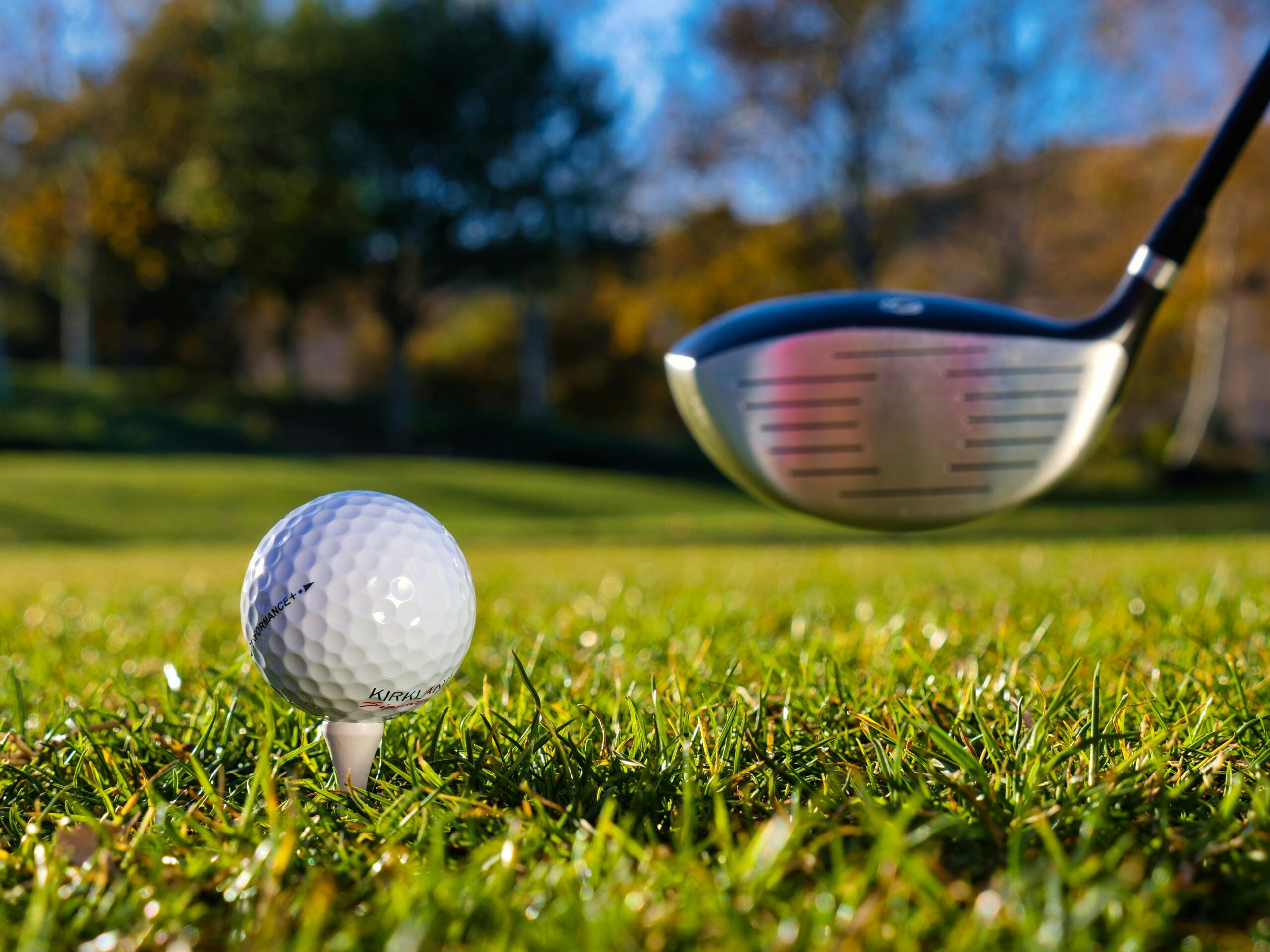 Close-up of a golf ball on a tee with a golf club in sunny weather on a grassy course.